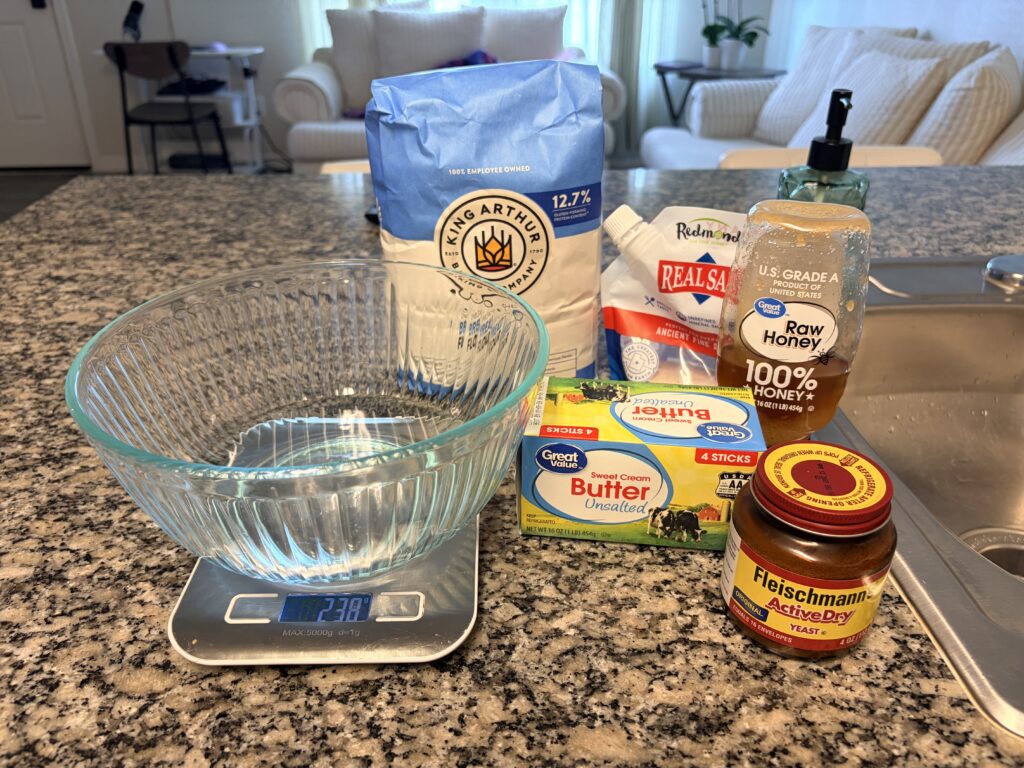 Ingredients for homemade white bread including bread flour, yeast, butter, honey, and salt.