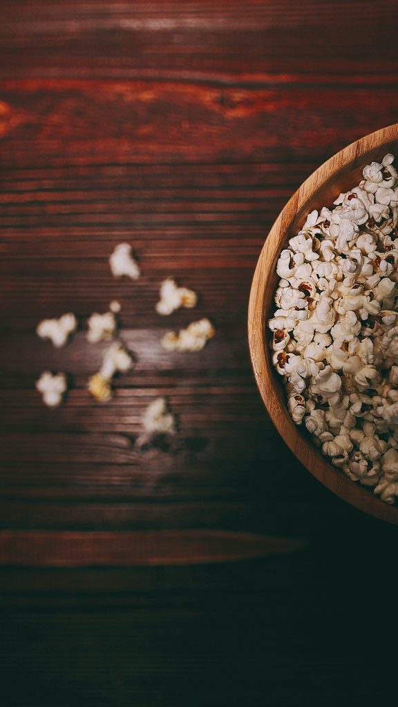 A wooden bowl filled with popcorn on a brown wooden table